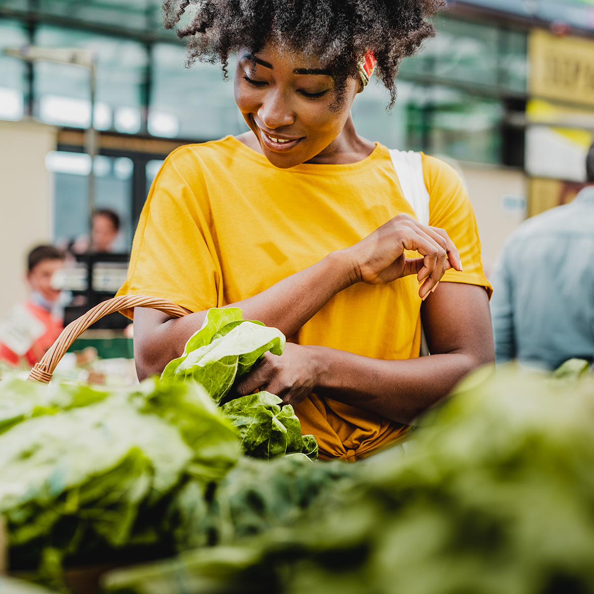 Mujer negra con camisa amarilla compra lechuga.